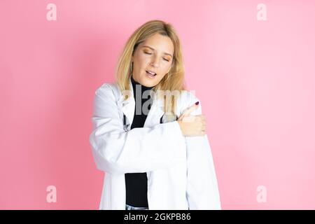 Jeune femme blonde médecin portant un stéthoscope debout sur fond rose isolé avec douleur sur son épaule et une expression douloureuse Banque D'Images