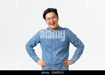 Joyeux jeune homme asiatique employé, collègue ayant la discussion, souriant heureux et regardant enthousiaste en parlant. Gars avec bretelles et lunettes Banque D'Images