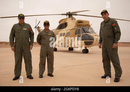 Un équipage d'aviation marocain prend une pause pour se poser devant un hélicoptère à Cap Draa, Maroc, le 12 juin 2021. L'équipage de l'Air a pris un visiteur distingué pour voir les zones d'entraînement African Lion 2021. African Lion 2021 est l'exercice annuel le plus important, conjoint et premier du Commandement de l'Afrique des États-Unis, organisé par le Maroc, la Tunisie et le Sénégal, le 7-18 juin. Plus de 7,00 participants de neuf pays et de l'OTAN s'entraînent ensemble en mettant l'accent sur l'amélioration de la préparation des forces américaines et des forces des pays partenaires. AL21 est un exercice multidomaine, multicomposant et multinational, qui emploie une gamme complète de capacités de mission Banque D'Images