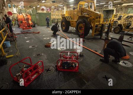 MER DES PHILIPPINES (15 juin 2021) des marins affectés au navire d’assaut amphibie déployé à l’avant USS America (LHA 6) testent des tuyaux d’incendie hydrostatiquement dans la zone d’entreposage des véhicules du navire. L'Amérique, navire chef de file du America Amphiobie Ready Group, ainsi que la 31e Marine Expeditionary Unit, opère dans la zone d'opérations de la 7e flotte des États-Unis pour améliorer l'interopérabilité avec les alliés et les partenaires et servir de force de réaction prête à l'emploi pour défendre la paix et la stabilité dans la région Indo-Pacifique. Banque D'Images