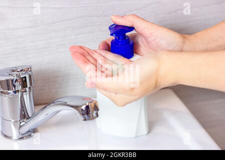 La jeune femme caucasienne se lave les mains avec de l'eau et du savon antiseptique liquide dans la salle de bains. Banque D'Images