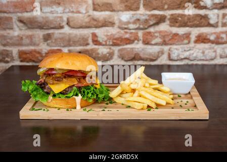 Hamburger au bœuf classique avec des oignons cuits, des cornichons, de la laitue, du fromage cheddar fondu, des tranches de tomates et du bacon fumé nappés de frites Banque D'Images