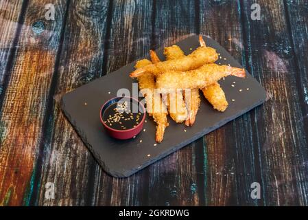 Crevettes géantes battues en manteau de pluie panko avec un bol de sauce soja et de graines de sésame sur une assiette en ardoise noire Banque D'Images