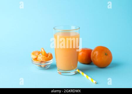 Verre de jus de mandarine, paille et ingrédients sur fond bleu Banque D'Images