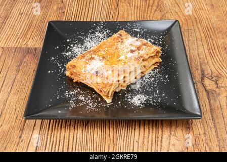 Recette de lasagnes rasée de porc avec beaucoup de fromage, beaucoup de couches de jambes et beaucoup de tomate sur une assiette carrée noire Banque D'Images