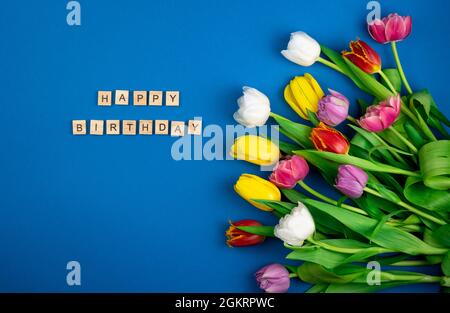 Joyeux anniversaire l'inscription en lettres de bois. Mélange de fleurs de tulipes de printemps. Arrière-plan avec fleurs tulipes gros plan différentes couleurs. Multi Banque D'Images