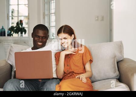 car african avec un ordinateur portable sur ses genoux est assis sur le canapé avec une femme Banque D'Images