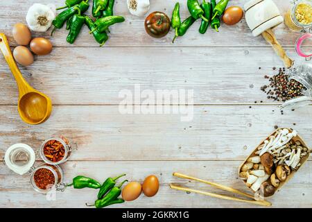 Vue de dessus image d'oeufs crus, poivrons verts, ail, cayenne et callène moulu, champignons et champignons, kumato tomate, graines de poivre sur table en bois Banque D'Images