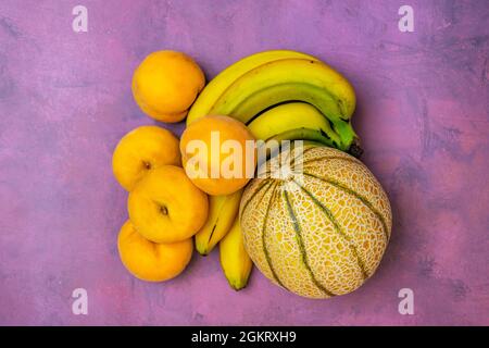 Petit melon Gaule avec bouquet de bananes et pêches jaunes sur fond rose Banque D'Images