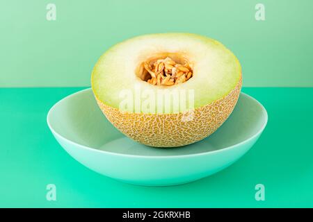 Melon Galia à moitié mûr avec les graines à l'intérieur sur une assiette bleue profonde et fond vert Uni Banque D'Images