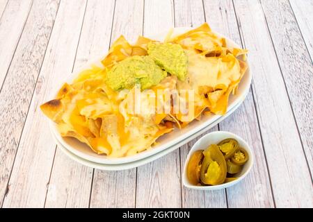 Recette de nachos de maïs avec guacamole, fromage fondu et tranches de jalapeno sur table blanche Banque D'Images