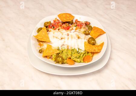 Recette de nachos avec guacamole et jalapenos, avocat, pico de gallo sur plaque blanche Banque D'Images