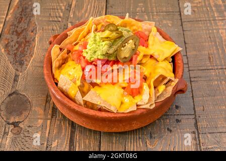 Incroyable recette mexicaine de nachos de guacamole dans un pot d'argile avec fromage cheddar fondu et jalapenos sur une table en bois Banque D'Images