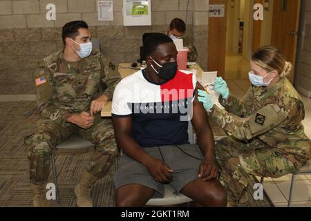 Le premier lieutenant Katelyn Harding (à droite), médecin adjoint au 1er Bataillon, 144e Régiment d'artillerie de campagne de la Garde nationale de l'Armée de Californie, administre un vaccin COVID-19 à un membre de la communauté de fort Irwin le 24 juin au Centre Dr. Mary E. Walker de fort Irwin, en Californie, à titre de SPC. Jacob Gutierrez (à l'extrême gauche), spécialiste des soins de santé avec 1st BN., 144th FA Regt., montres. Harding, un natif de San Diego, Gutierrez, un natif de Rancho Cucamonga, et d'autres personnels médicaux avec 1st BN., 144th FA Regt. A augmenté l'événement de vaccin COVID-19 organisé par l'hôpital communautaire de l'armée de Weed. Banque D'Images