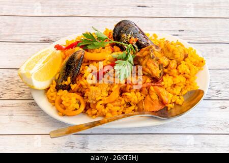 Tapa de paella mélangée avec rondelles de poulet et de calmar, moules, safran, poivre et tranche de citron sur table en bois Banque D'Images