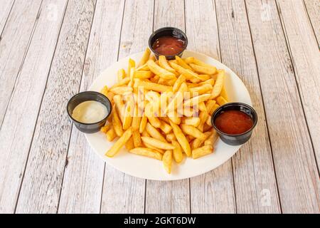 Hors-d'œuvre de montagne frites avec sauces variées sur plaque blanche et table en bois clair Banque D'Images