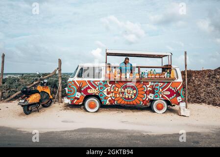 Chef cuisinant dans son camion alimentaire coloré en face de la plage à côté d'un scooter stationné Banque D'Images