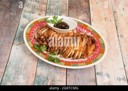 Rôti de canard entier avec une peau croustillante, servi dans des filets avec une sauce pour l'accompagner cuit dans un restaurant chinois et placé sur un fond de bois Banque D'Images
