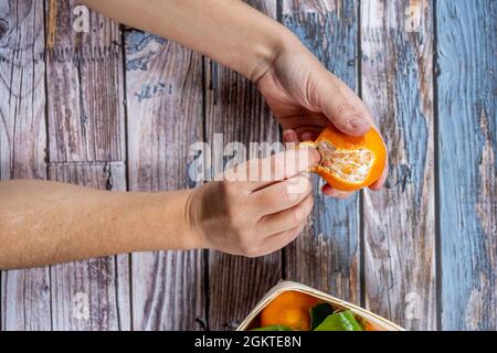 Les mains de femme peeling mandarine laissant les segments en vue sur table en bois de tons bleus et de peinture peeling Banque D'Images