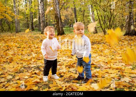 Les enfants gais attrapent des feuilles d'érable tombant dans le parc de la ville d'automne Banque D'Images