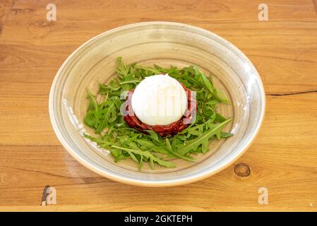 Salade burrata puglia typique avec arugula, un lit de tomates déshydratées étalées d'huile d'olive sur une assiette grise profonde Banque D'Images