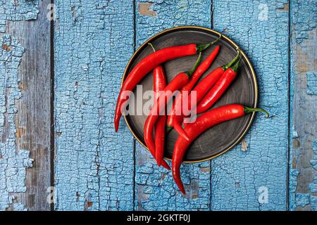 Plaque métallique circulaire vintage avec anneau doré et piments rouges sur une table en bois bleu Banque D'Images
