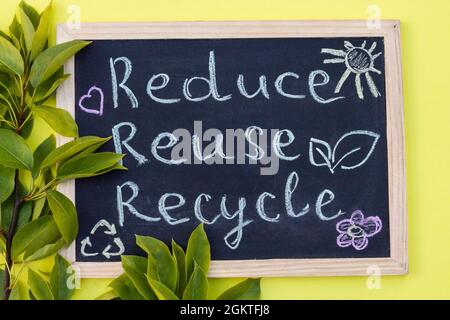 Tableau à craie affiche de réutilisation du recyclage sur fond jaune avec des feuilles vertes. Vue de dessus Banque D'Images