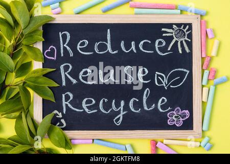 Tableau à craie affiche de recyclage Reuse sur fond jaune avec feuilles vertes et craies. Vue de dessus Banque D'Images