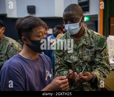 Hôpital Corpsman 2e classe Yves Giraneza, affecté à la clinique de santé de la branche de Yokosuka de l'hôpital naval américain Sasebo, fournit une carte documentant la vaccination à un employé local affecté à l'installation de réparation de navires de la marine américaine et au détachement du centre de maintenance régional du Japon, au cours de la distribution du vaccin au commandant, Activités de la flotte Théâtre Showboat de Sasebo le 30 juin 2021. Avec l'autorisation du gouvernement du Japon, le CFAS a commencé à administrer des vaccins aux employés du MLC, de l'IHA et de MC en juin 23. Banque D'Images