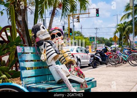 Des squelettes sculptant sur un banc en bois avec un vélo stationné sur la route de la ville Banque D'Images