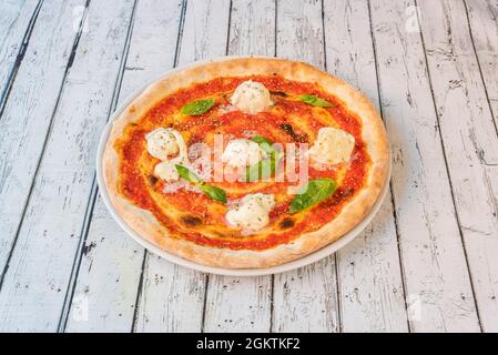 Pizza à Margarita pour le petit déjeuner avec des boulettes de fromage de buffle gratinées, des feuilles de tomate et de basilic sur une table blanche Banque D'Images