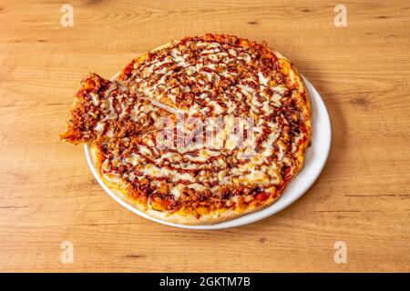 Pizza avec sauce barbecue en cercles avec beaucoup de viande hachée, beaucoup de fromage fondu et une tranche coupée sur une assiette blanche Banque D'Images