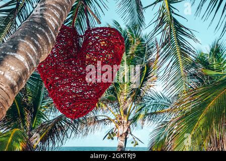 Décoration en forme de coeur rouge accrochée à la noix de coco en face de la mer Banque D'Images