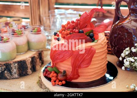 Gâteau orange décoré de baies de rowan, de raisins de Corinthe et de hanches roses. Fragment d'une table douce dans un style rustique. Banque D'Images