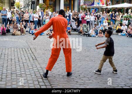 Un artiste de rue ou un interprète de rue joue avec un enfant, sélectionné dans la foule d'observation, et les deux dansent la soie dentaire Banque D'Images