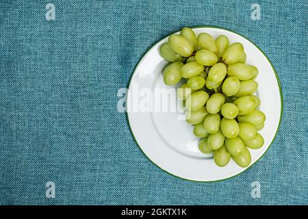 Assiette en grappe de délicieux raisins blancs de dessert sur un tissu vert vu du dessus Banque D'Images