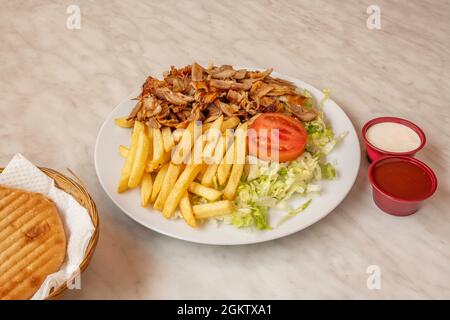 Menu de kebab de viande de poulet avec frites, salade iceberg, sauce tomate, sauce yaourt et sauce tomate et pain pita sur table en marbre blanc Banque D'Images