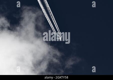 Avion volant quittant les contrailles dans le ciel bleu avec des nuages. Banque D'Images