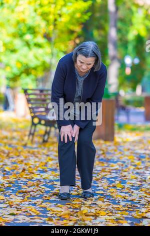 Senior woman having douleur au genou walking in park Banque D'Images