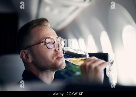 Voyages d'affaires en avion. Homme regardant à travers la fenêtre et buvant du champagne pendant le vol. Banque D'Images