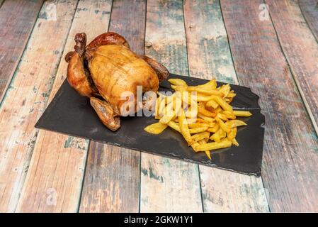 Rôti de poulet sur une brochette rotative avec une peau très croustillante accompagnée d'une garniture de chips maison sur une plaque d'ardoise Banque D'Images