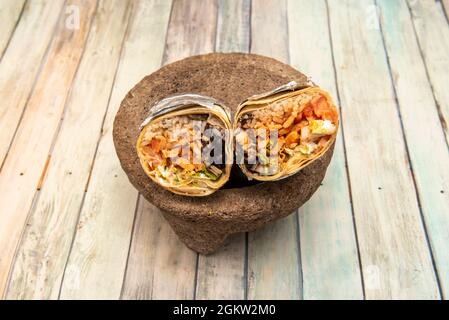 Grand burrito de poulet grillé à l'intérieur d'une molajete en pierre volcanique grise sur une table en bois Banque D'Images