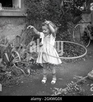 Années 1960, historique, à l'extérieur sur un chemin de jardin, une petite fille jouant avec un hula hoop, un jouet hoop qu'elle tourne autour de sa taille, Allemagne.Bien qu'un cerceau existe et utilisé par des enfants depuis des centaines d'années - mais pas connu sous ce nom - ce n'est qu'à la fin des années 1950, quand la version en plastique a été introduite, que la folie pour eux a pris le dessus.Le hula hoop - le nom qui vient il est dit de faire la Hula, la danse à Hawaï - est devenu une grande mode, avec plus de 100 millions vendus en deux ans.Jusqu'à la fin des années 1970, au début des années 1980, les hula Hoops demeuraient un jouet populaire pour enfants. Banque D'Images