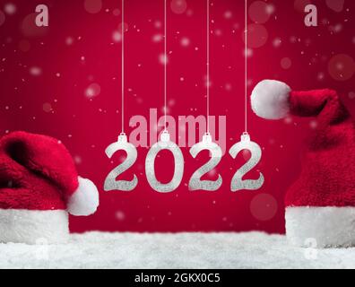 Deux chapeaux de père Noël sur neige sur fond rouge, décoration de Noël. Concept de vacances. 2022. Banque D'Images