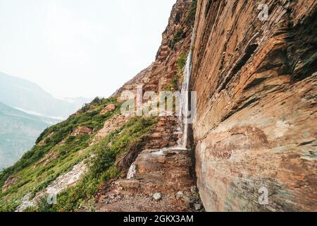 Cascade sur l'édifice de la falaise et sentier le long du sentier du glacier Grinnell. Les randonneurs doivent traverser la chute d'eau Banque D'Images