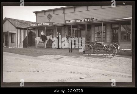 Chloride, Arizona, 1915 ans, femme sur un cheval blanc et homme debout près d'elle devant un marché de la viande et un restaurant. Inage de 3 x 5 pouces négatif nitrate. Banque D'Images