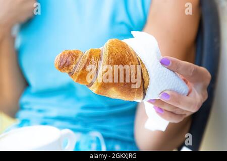 Femme caucasienne en t-shirt blu tient à la main croissant maison frais avec chocolat. Petit déjeuner italien à l'extérieur. Nutrition et régime. Concept Banque D'Images