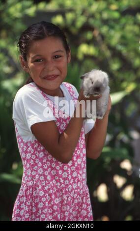 Austin Texas USA,1995: Fille hispanique de 9 ans tient doucement son lapin de lapin d'animal de compagnie dans l'arrière-cour de sa famille. M. EC-0089 ©Bob Daemmrich Banque D'Images