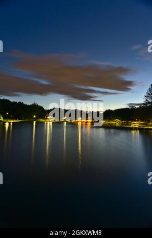 Vue verticale d'une longue exposition du lac Beaver, Mont-Royal, Montréal, QC, Canada à l'heure bleue au crépuscule, par une journée d'été nuageuse. Les lumières et l'arbre Banque D'Images