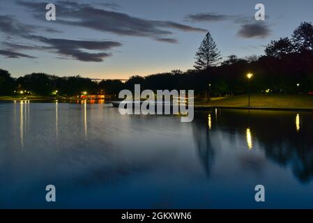 Une longue exposition du lac Beaver, Mont-Royal, Montréal, QC, Canada à l'heure bleue au crépuscule, par une journée d'été nuageuse. Les lumières et les arbres réfléchissent sur la Banque D'Images